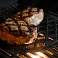 medl-Winter-Grillen, Mülheim an der Ruhr Auf einem Grillrost liegen zwei saftige Steaks mit Grillstreifen, von der Hitze darunter beleuchtet.