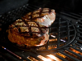 medl-Winter-Grillen, Mülheim an der Ruhr Auf einem Grillrost liegen zwei saftige Steaks mit Grillstreifen, von der Hitze darunter beleuchtet.