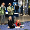 Weihnachtlicher Familiennachmittag_nbz-Alfsee.jpg Drei Erwachsene beobachten Kinder, die auf einem großen, blauen Bodenplan in einem Ausstellungsraum spielen.Three adults watch children playing on a large blue floor plan in an exhibition room.Tre voksne ser på børn, der leger på en stor blå gulvplan i et udstillingsrum.Drie volwassenen kijken naar spelende kinderen op een grote blauwe plattegrond in een tentoonstellingsruimte.