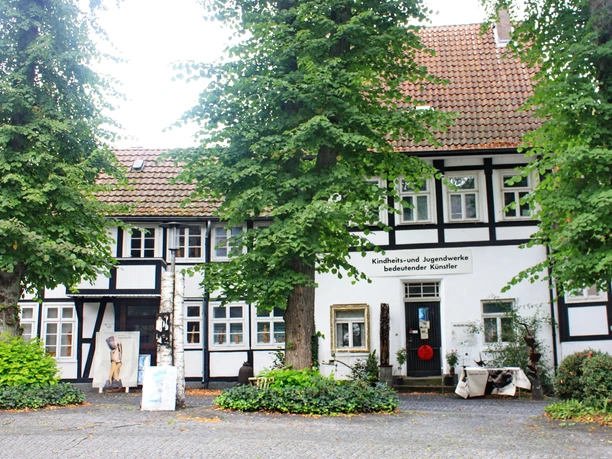 Kindheits Museum.JPG Fachwerkhaus mit großen Fenstern, umgeben von hohen Bäumen und gepflastertem Gehweg im Vordergrund.
