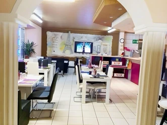 Pizza Kurier Steinhagen Restaurant mit moderner Einrichtung, weißen Tischen, schwarzen Stühlen und rotem Tresen im Vordergrund.