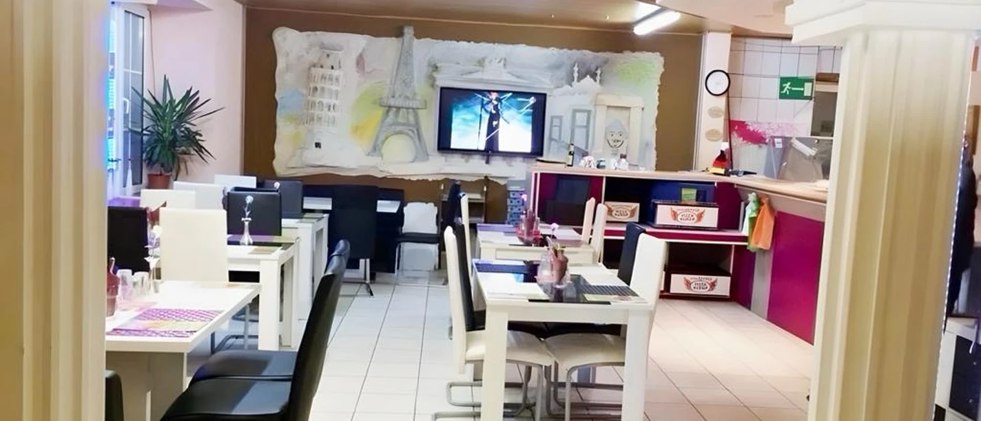 Pizza Kurier Steinhagen Restaurant mit moderner Einrichtung, weißen Tischen, schwarzen Stühlen und rotem Tresen im Vordergrund.