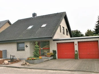 Ein zweigeschossiges Einfamilienhaus mit weißen Klinkerwänden und zwei roten Garagentoren.