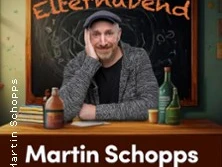 Titel: Martin Schopps Soloprogramm "Elternabend". Der Künstler sitzt gelassen vor einer Tafel.