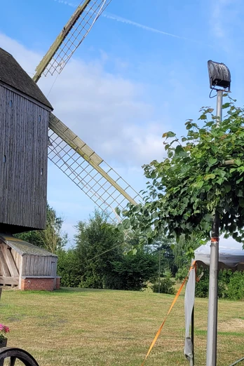 Bockwindmühle Wehe Historische Bockwindmühle Wehe auf grüner Wiese, umgeben von Blumen und Bäumen unter blauem Himmel.