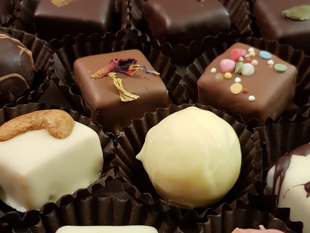 Pralinen_dunkel.jpg Verschiedene Pralinen mit bunten Dekorationen und vielseitiger Schokoladenverzierung sind zu sehen.