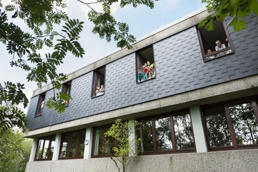 Jugendherberge Lindlar Moderne Schulgebäude-Fassade mit Kindern, die aus den geöffneten Fenstern im oberen Stockwerk schauen.