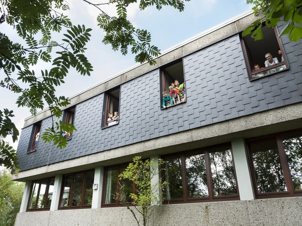 Jugendherberge Lindlar Moderne Schulgebäude-Fassade mit Kindern, die aus den geöffneten Fenstern im oberen Stockwerk schauen.