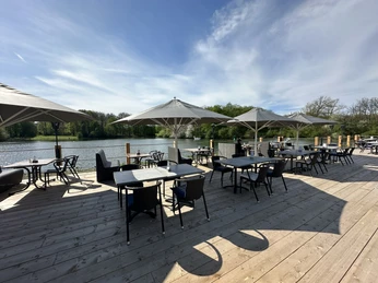 Terrasse2 Terrasse mit Holzboden, Sitzmöglichkeiten, aufgespannten Schirmen und Blick auf den SeeTerrace with wooden floor, seating, stretched umbrellas and a view of the lake