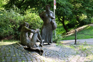 Eine Marktfrau als Bronzefigur steht neben einer sitzenden Bronzefigur, die den Teufel darstellt.