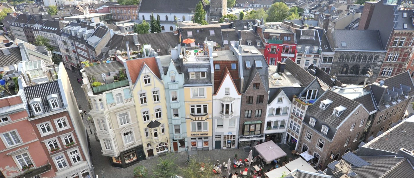 Öffentliche Architekt(o)ur Führung in Aachen Blick von oben auf einen Teil des Münsterplatzes mit Außengastronomie und schmalen Reihenhäusern mit spitzen Dächern.