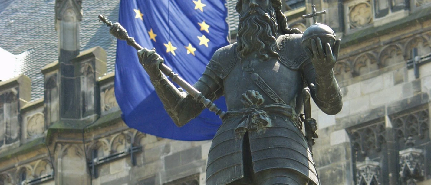 Eine Statue von Kaiser Karl dem Großen in Rüstung vor dem Aachener Rathaus und einer Europaflagge.