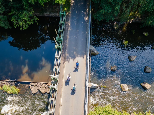 Emsbrücke bei Harsewinkel Luftaufnahme der Emsbrücke mit Radfahrern, umgeben von Bäumen und fließendem Wasser darunter.