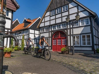Radfahrende genießen einen sonnigen Tag vor Fachwerkhäusern in einer malerischen Stadtumgebung.