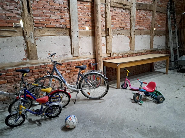 Bicycles and children's toys are stored in a rustic barn with exposed brickwork.