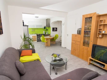 Moderne Wohnung mit grauem Sofa, bunter Deko, Wohnwand, offener Küche in Weiß und Grün.