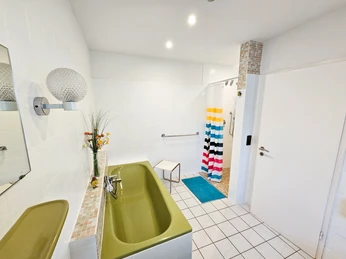 Helle, barrierefreie Küche mit grüner Arbeitsplatte, buntem Duschvorhang und modernen Armaturen.