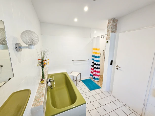 Helle, barrierefreie Küche mit grüner Arbeitsplatte, buntem Duschvorhang und modernen Armaturen.