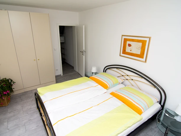 Helles Schlafzimmer mit Doppelbett, farbenfroher Bettwäsche, großem Kleiderschrank und Kunst an der Wand.