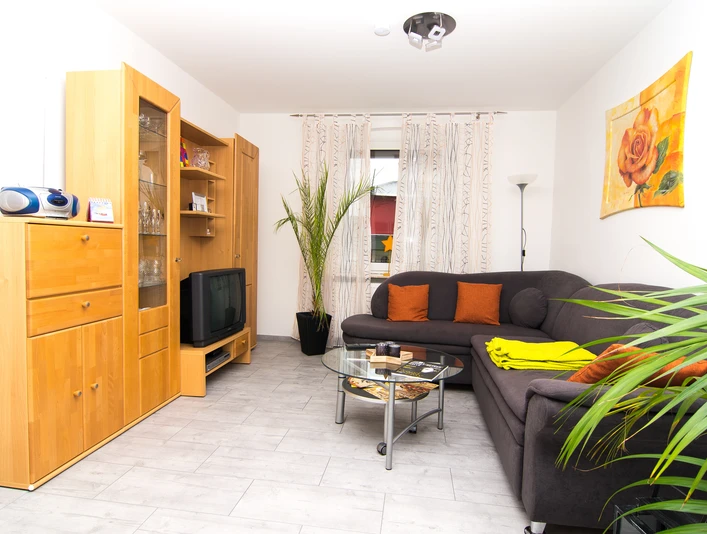 Modern eingerichteter Wohnbereich mit hellen Holzmöbeln, grauem Ecksofa, Glassofatisch und Pflanzen.