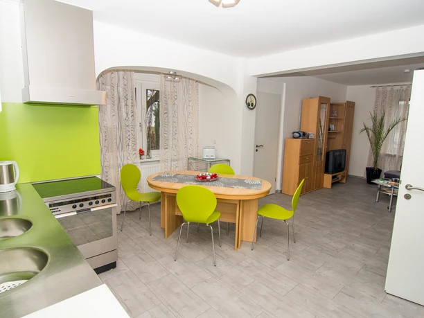 Moderner Wohn-Ess-Bereich mit Holztisch, grünen Stühlen, angrenzende Küche mit heller Wandfarben.