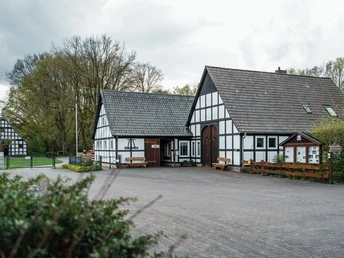 Historische Fachwerkgebäude umgeben von Bäumen, mit Informationstafel und einladendem Vorplatz.
