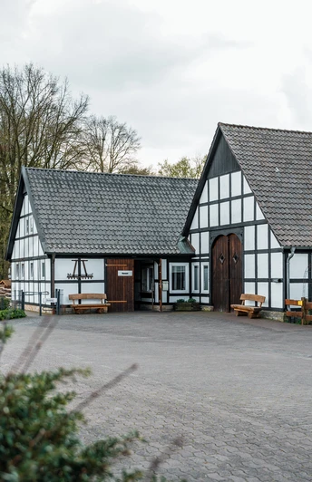Historische Fachwerkgebäude umgeben von Bäumen, mit Informationstafel und einladendem Vorplatz.