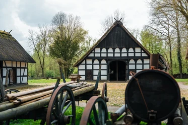 Historischer Bauernhof mit Fachwerkgebäuden und landwirtschaftlichen Maschinen im Freilichtmuseum.