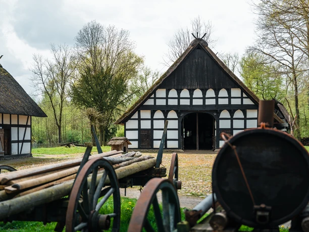 Historischer Bauernhof mit Fachwerkgebäuden und landwirtschaftlichen Maschinen im Freilichtmuseum.