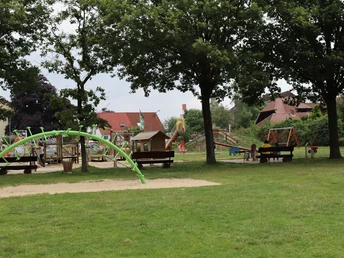 Spielplatz Museumshof Spielplatz mit Klettergerüst, Schaukeln und Rasenflächen umgeben von großen Bäumen, ideal für Familien.