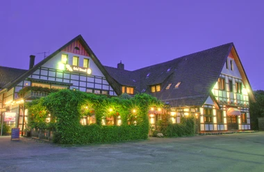 Hotel Vivendi Herford - Außenansicht.jpg Fachwerkhotel mit beleuchteter Fassade, vor dörflicher Kulisse in der Dämmerung, begrüntes Vorhaus.