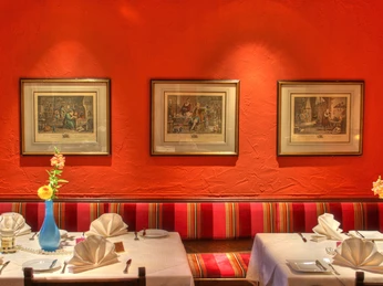 Ein elegant gedeckter Tisch in einem Restaurant vor einer warmen, orangefarbenen Wand mit Kunstwerken.