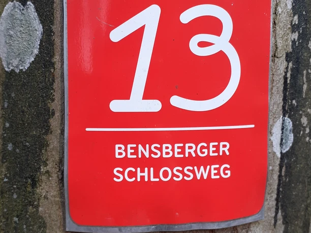 Wegweiser des Bensberger Schlosswegs, Route 13, auf einer Baumrinde in Bergisch Gladbach.
