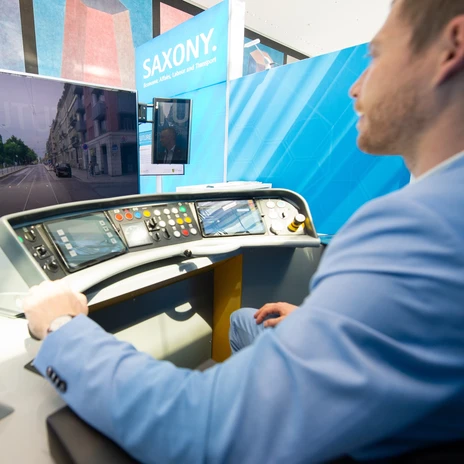 Saxony stand of the International Transport Forum (ITF) | Leipzig Convention Bureau A participant drives a tram simulator at the Saxony stand in the exhibition hall during the Annual Summit of the International Transport Forum (ITF) on “Transport for Inclusive Societies” - presented by Leipzig Convention Bureau