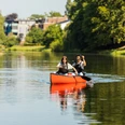 herford-kanu-teutoburger-wald-tourismus-h-tornow-017-jpg.jpg Zwei Personen paddeln entspannt in einem roten Kanu auf einem ruhigen Fluss, umgeben von Natur und Bäumen.