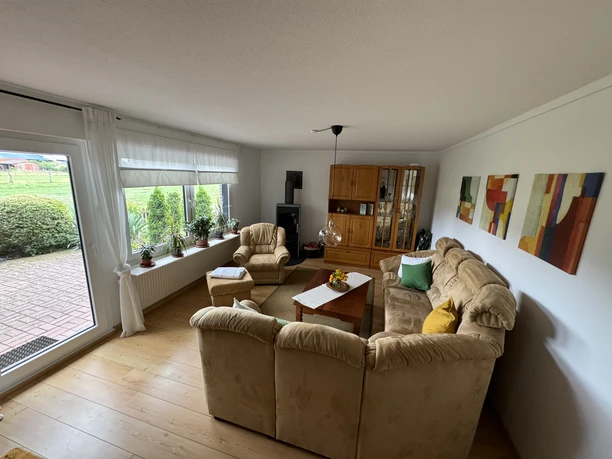 Idylle zwischen Weser und Moor Helles Wohnzimmer mit beigefarbenen Sofas, Holzmöbeln und modernen Gemälden, Blick auf die Terrasse.