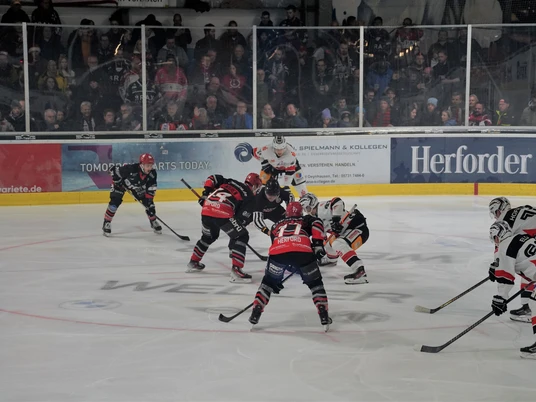 Herford-Ice-Dragons-Spiel- 2-Jana-Hemmelmann.jpg Eishockeyspiel der Herford Ice Dragons in Aktion, Spieler kämpfen mit Dynamik um den Puck auf dem Eis.