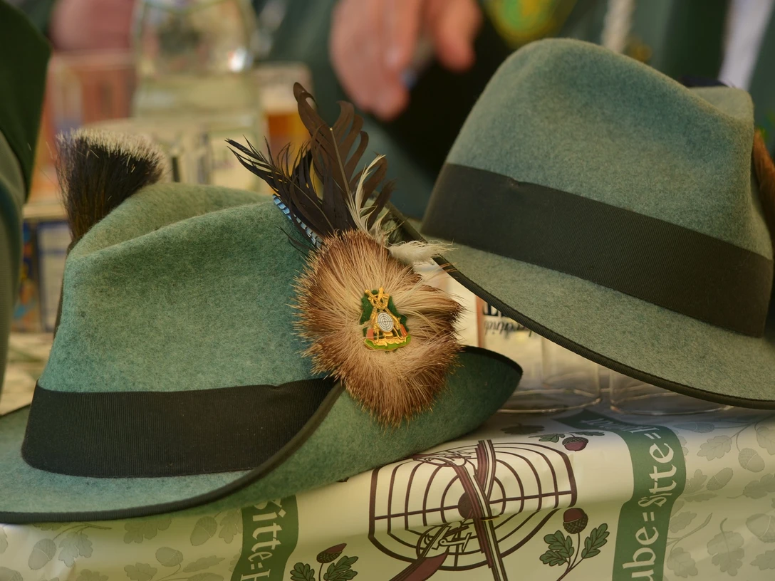 Grüne Filzhüte mit schwarzer Kordel und Federbrosche, Symbol traditioneller bayerischer Tracht.