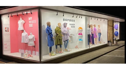 BSPNGN-FASHIONROOM.jpg Nachtaufnahme eines Schaufensters mit modischer Bekleidung und farbigen Wanddisplays.