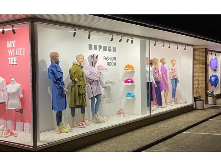 BSPNGN-FASHIONROOM.jpg Nachtaufnahme eines Schaufensters mit modischer Bekleidung und farbigen Wanddisplays.
