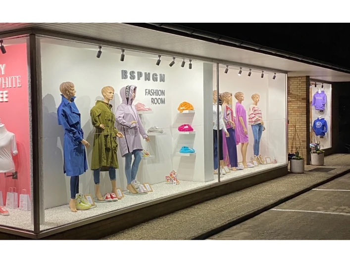 BSPNGN-FASHIONROOM.jpg Nachtaufnahme eines Schaufensters mit modischer Bekleidung und farbigen Wanddisplays.
