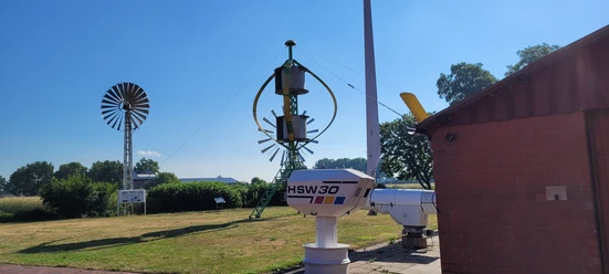 Deutsches Windkraftmuseum Windkraftmuseum mit alten Windturbinen und technischen Anlagen auf einer Wiese bei blauem Himmel.