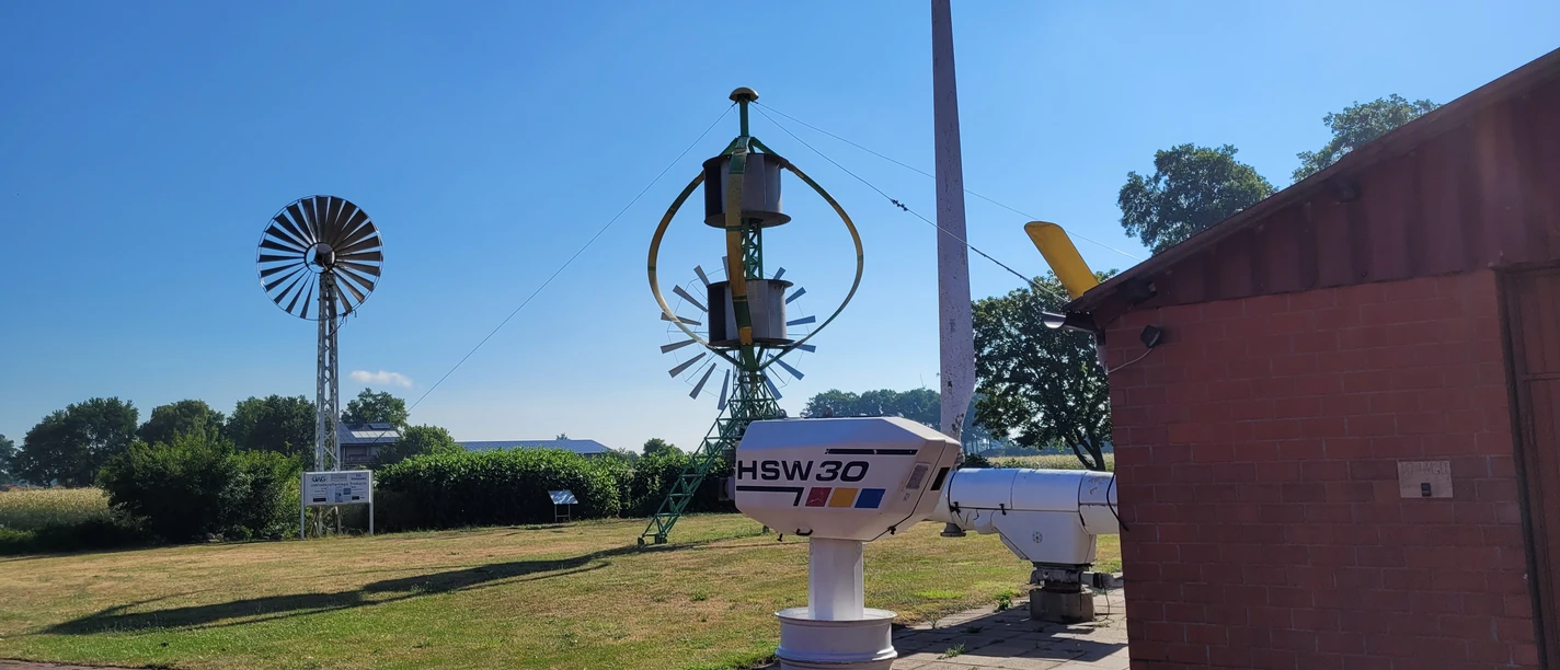 Deutsches Windkraftmuseum Windkraftmuseum mit alten Windturbinen und technischen Anlagen auf einer Wiese bei blauem Himmel.