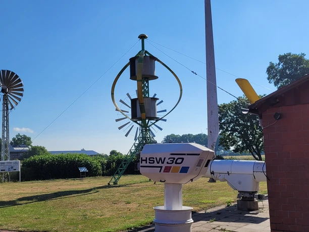 Deutsches Windkraftmuseum Windkraftmuseum mit alten Windturbinen und technischen Anlagen auf einer Wiese bei blauem Himmel.
