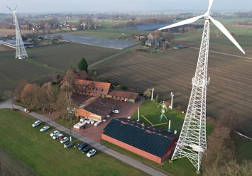 Drohnenaufnahme Windkraftmuseum Luftaufnahme des Windkraftmuseums mit großen Windrädern in ländlicher Umgebung und Solarpanels.
