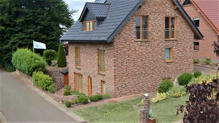 FeWo Herford-Aussenansicht.jpg Ferienwohnung in rotem Backsteingebäude mit schrägem Dach, gepflegtem Garten und Weg an ruhiger Straße.