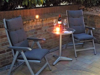 Zwei gepolsterte Gartenstühle an einem Rundtisch mit Kerzen und Wein auf einer gepflasterten Terrasse.