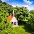 Altenheerse-Himmelsbergkapelle-4.jpg Eine kleine Kapelle mit rotem Dach und grünem Turm umgeben von blühenden Kastanienbäumen.