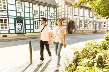 herford-altstadt-teutoburger-wald-tourismus-h-tornow-003-jpg.jpg Ein Paar spaziert an Fachwerkhäusern in einer sonnigen Altstadt, umgeben von grüner Vegetation.