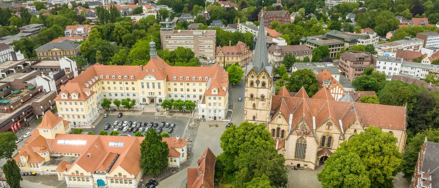 Luftaufnahme des Herforder Rathausplatzes mit der gotischen Kirche und umliegenden Gebäuden im Grünen.
